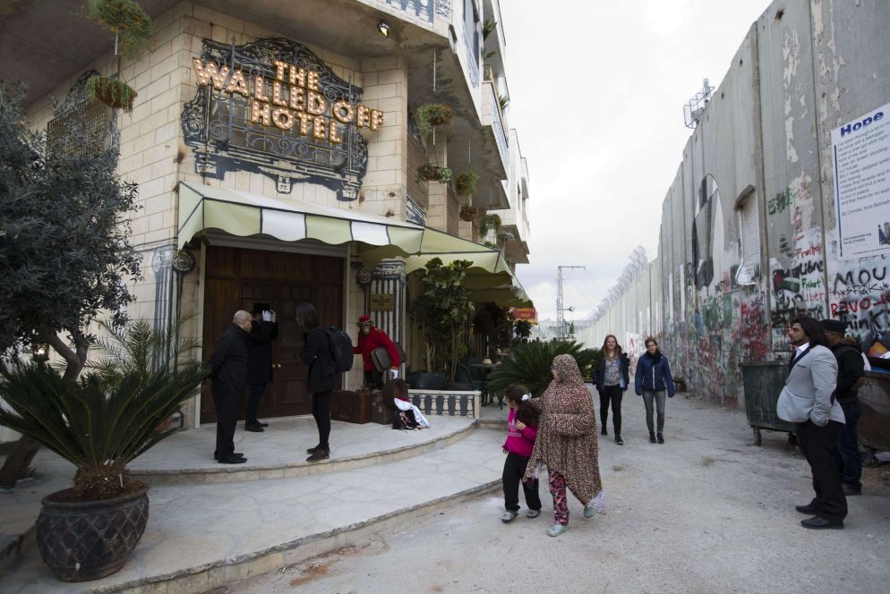 Persone davanti al The Walled Off Hotel a destra si vede il muro di separazione tra la Cisgiordania e Israele