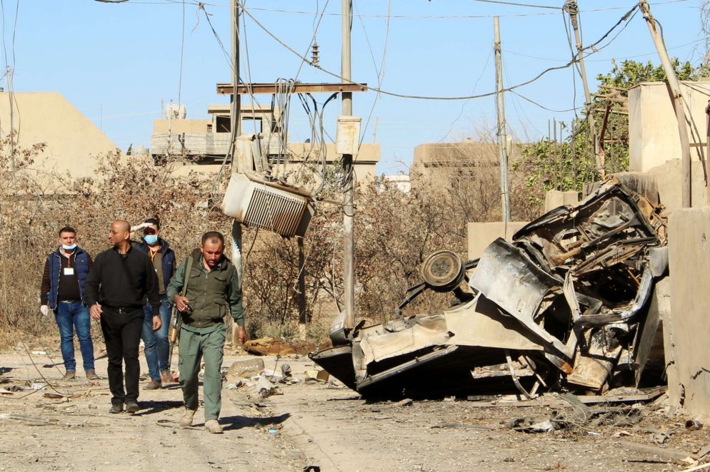 Un sacerdote in una via di fianco a una macchina distrutta da un colpo di mortaio