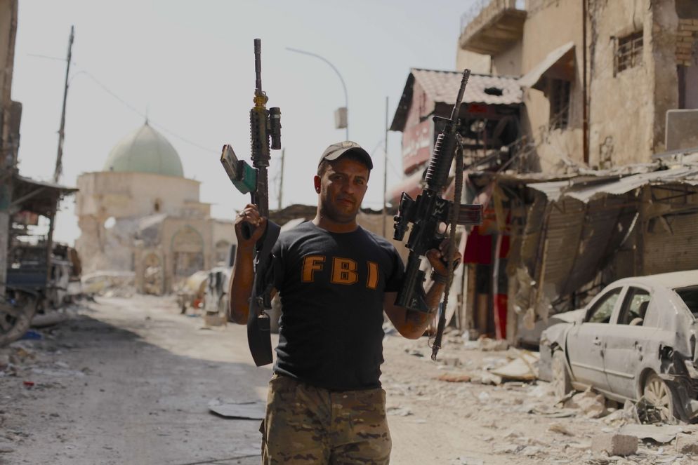 Soldato della seconda brigata del 16esimo battaglione della Golden Division fa picchetto nelle strade davanti la moschea al Nouri e mostra orgoglioso due dei 1500 fucili automatici sequestrati nel deposito di munizioni e armi di Daesh in città vecchia