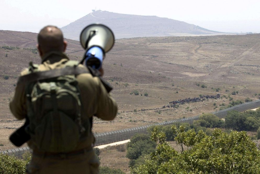 Un soldato israeliano con un altoparlante comunica con i profughi siriani. Non devono avvicinarsi troppo al muro (Ansa)