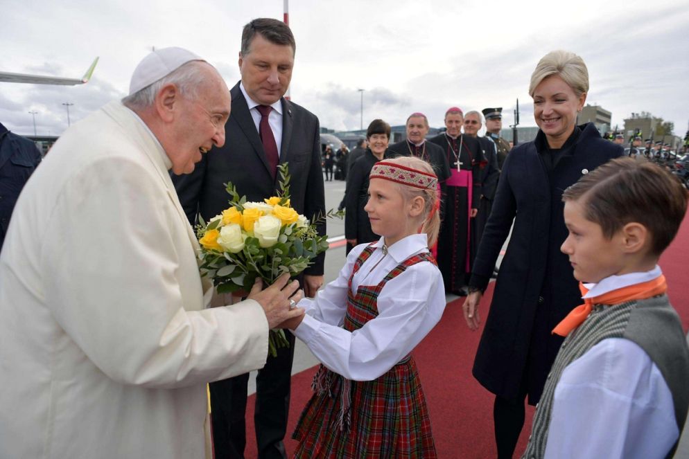 All'aeroporto il Papa è stato accolto con un mazzo di fiori consegnatogli da bambini in costume lettone. Accanto a lui il presidente Vejonis (Ansa)