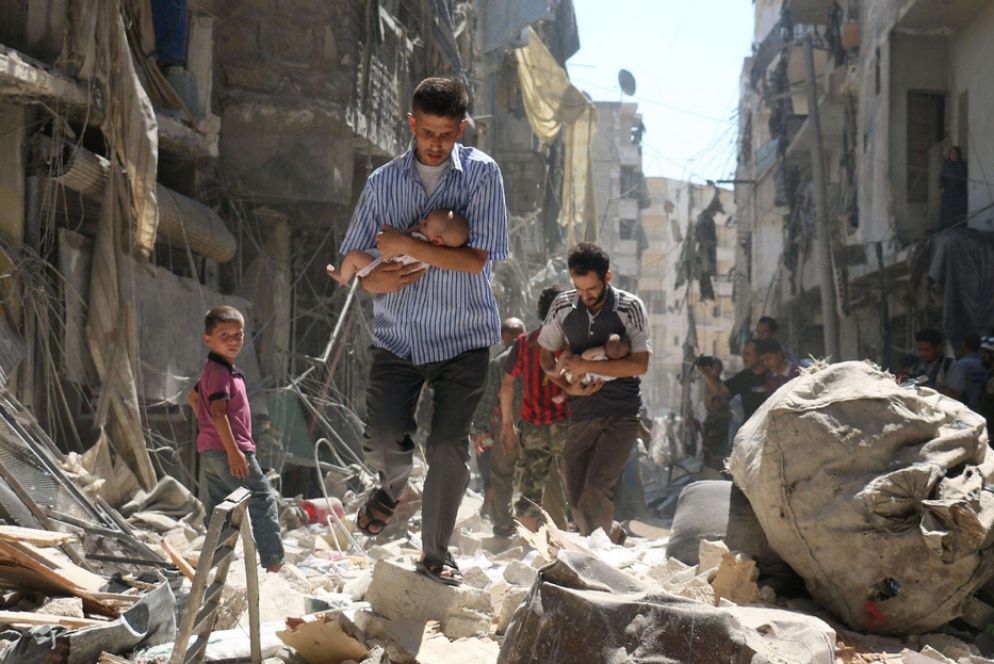 Padri - Due uomini, in una pausa di uno dei quotidiani bombardamenti, portano in salvo i bimbi neonati nel quartiere di Salihin nella periferia settentrionale di Aleppo: l’assedio alla città è divenuto simbolo della guerra in Siria