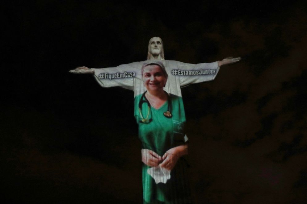 Tra le grandi braccia aperte del Cristo Redentore viene proiettata l'immagine di un'infermiera