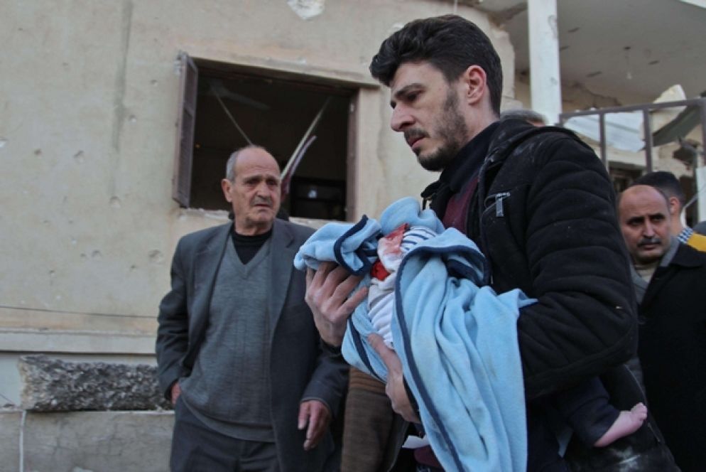 Un uomo trasporta il corpo di un bambino dopo un attacco aereo a Maarrat Misrin nel Nord Est della provincia di Idlib - Ansa