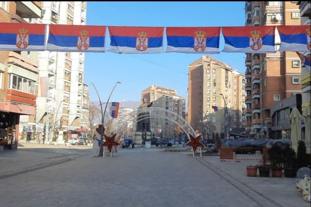 La via principale della parte serba di Kosovska Mitrovica, dove alle bandiere serbe si aggiungono gli addobbi natalizi. Sullo sfondo, la statua di Lazar Hrebeljanović, eroe della battaglia di battaglia di Kosovo Polje, rivolta verso la parte albanese