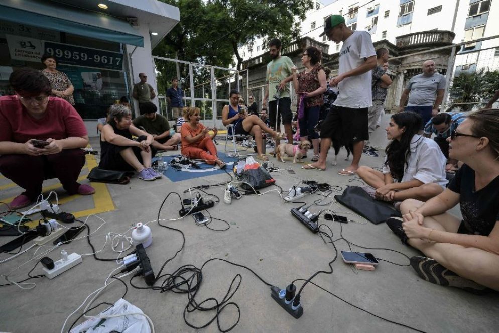 Persone caricano i loro telefoni cellulari fuori da una farmacia nel centro storico di Porto Alegre