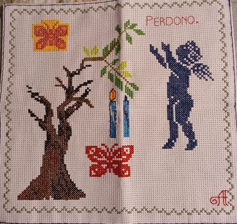 Il ricamo rappresenta il perdono. L’albero di ulivo i bruciato è Antonio, con un passato che ha bruciato la sua vita e molte vite. Dopo l’incontro con “il nemico” che uccise suo fratello Salvatore nasce un virgulto verde che rappresenta la nuova vita. Le due candele: quella accesa è l’odio, il rancore, il desiderio di vendetta, quella spenta è l’amore, l’illuminazione della ragione, nell’incontro tra le due candele si genera una nuova luce che ha il sopravvento sulla luce precedente alimentata dalla vendetta. Le due farfalle rappresentano la leggerezza che nasce dal perdono di una persona sgravata dalla pesantezza del desiderio di vendetta. L’angelo rappresenta Dio.