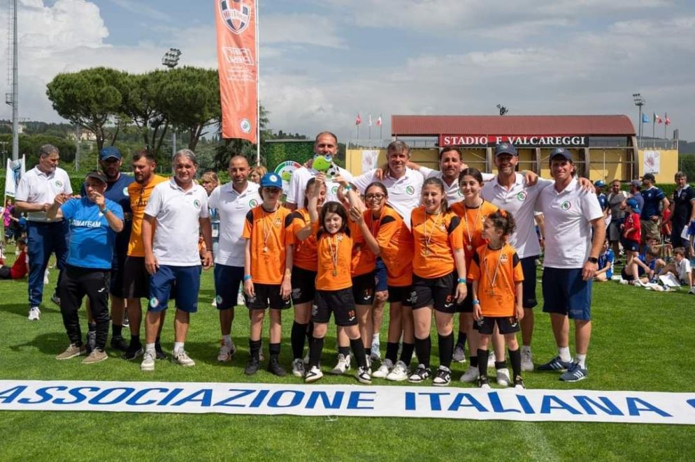 Le ragazze arancionero della Dimateam a Coverciano durante la Junior Cup, mentre sollevano il trofeo dell'Associazione italiana calciatori. - Cortesia dell'Asd Dimateam